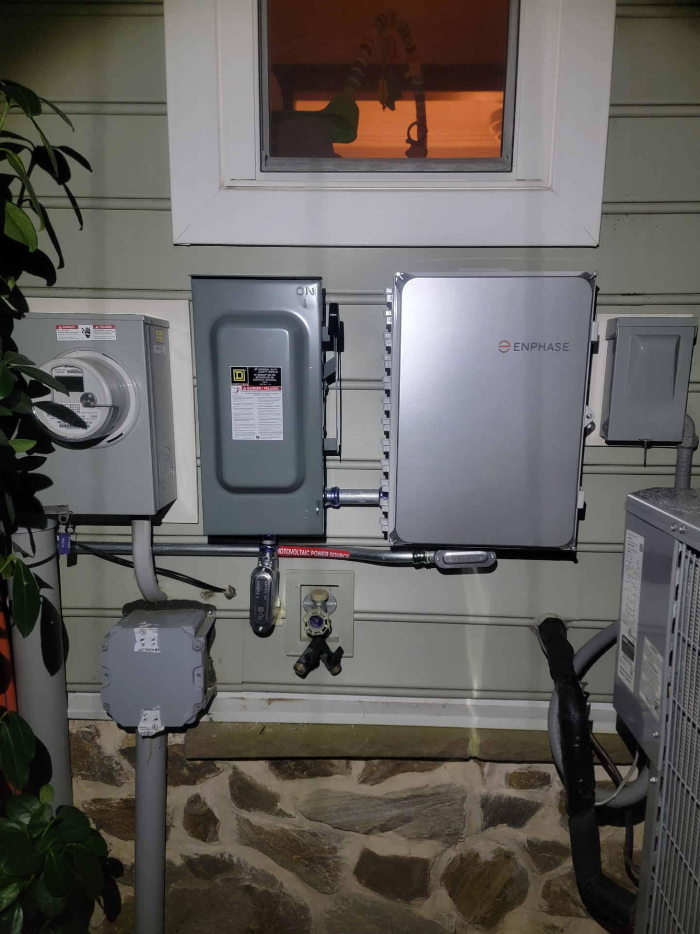 Enphase combiner box installed beside the utility meter and AC disconnect on a home exterior